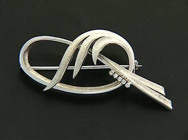 LOTTO 16a SPILLA ANNI '70 CA. In oro bianco 18 kt realizzata a volute incrociate incise con motivo a cinque diamanti taglio huit-huit per tot. cts. 0,10 ca., chiusura ad ago semplice. Gr 8,20; dim. cm 5,5x2,3.