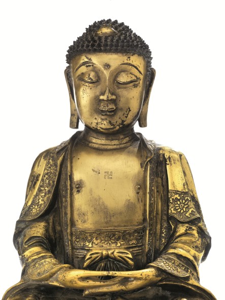 Lotto 36 € 20.000 / 30.000 BUDDHA, CINA, DINASTIA MING, SECC. XVI-XVII in bronzo dorato, la figura seduta in dhyanasana con mani giunte in dhyana mudra, elegantemente vestito con una veste monastica fermata al centro con un fiocco, i bordi della veste finemente cesellati, il petto inciso con l'emblema della svastica, il volto dall’espressione serena con sopracciglia molto accentuate e labbra sorridenti, alt. cm 41, poggiante su base in legno 