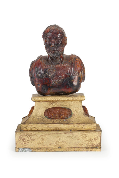1285. BUSTO IN AMBRA, XVIII SECOLO raffigurante probabilmente un imperatore romano, basamento ornato da tre camei in ambra a plinto in legno rivestito in lamina di ottone incisa a motivi floreali e vegetali stilizzati; usure, alcune rotture e mancanze, restauri Alt. cm 15,5, larg. cm 12, prof. cm 5,5 Con basamento, alt. cm 27 Stima € 2.000 - 3.000 Aggiudicazione € 49.600 