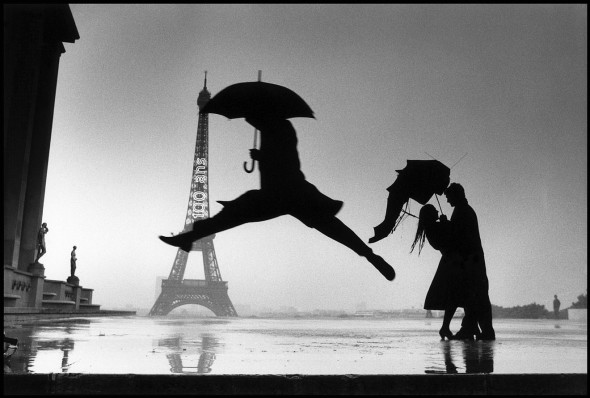 Elliott Erwitt Man with umbrella jumping over puddle in front of the Eiffel tower