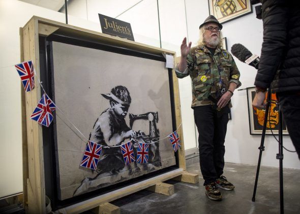 Ron English standing in front of a Banksy mural he recently bought and plans to whitewash as an act of protest. Photo by Barbara Davidson/Getty Images.