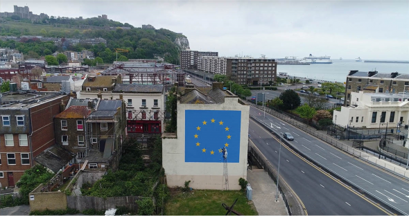 murale di Banksy con la bandiera euroea visto da lontano con lo sfondo del porto