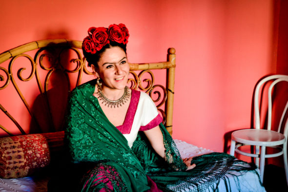 Un'attrice impersonifica Frida Kahlo seduta sul letto